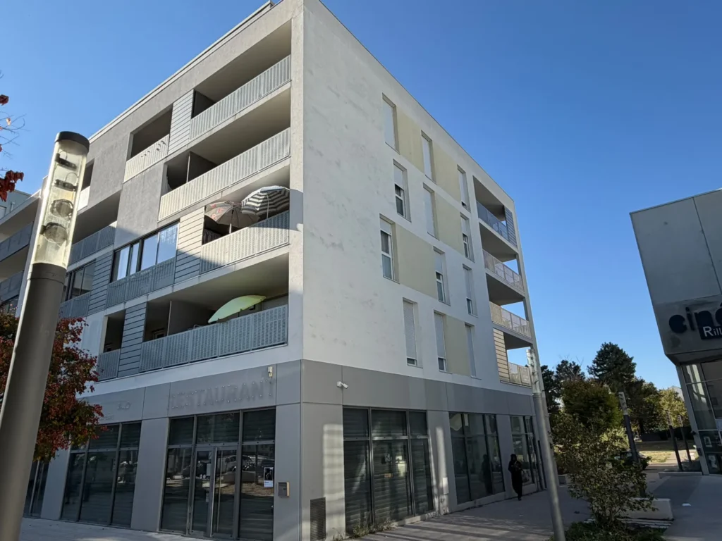 La façade de la résidence : un immeuble récent avec balcons, commerces en rez-de-chaussée.